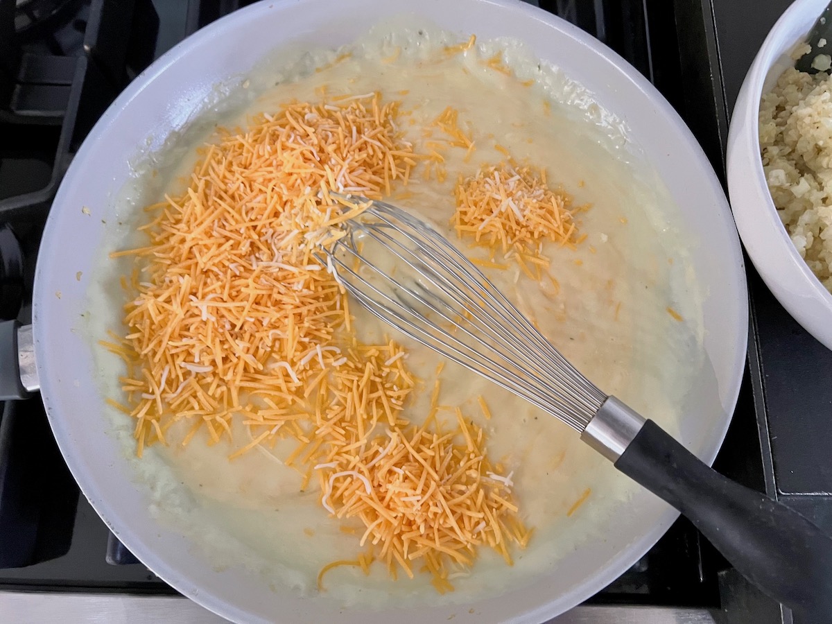 Shredded cheddar added to thickened sauce in a frying pan Cheesy Cauliflower Rice Recipe.