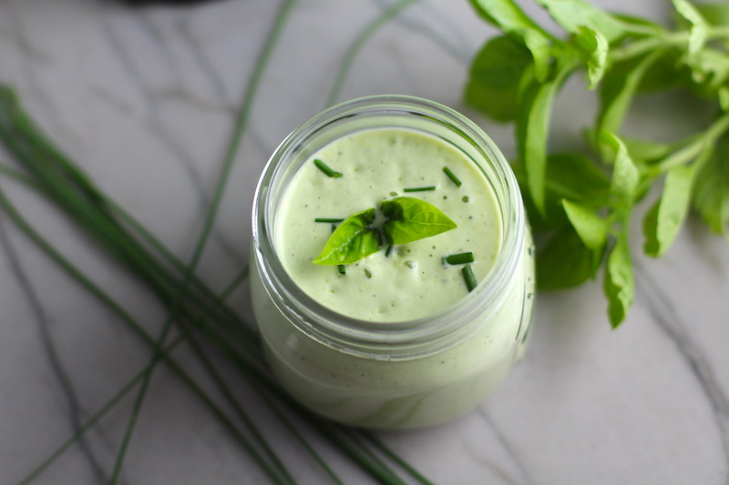 Basil & Chive Yogurt Dressing in a jar on counter with basil leaves and chives on top and on the counter. This dressing with Lemon and Honey is creamy, light, savory, and a little bit sweet. It takes only minutes to make this delicious homemade dressing.  Basil & Chive Yogurt Dressing is perfect for salads, for drizzling over roasted veggies, steak, chicken, or fish, and amazing for dipping fries into!!