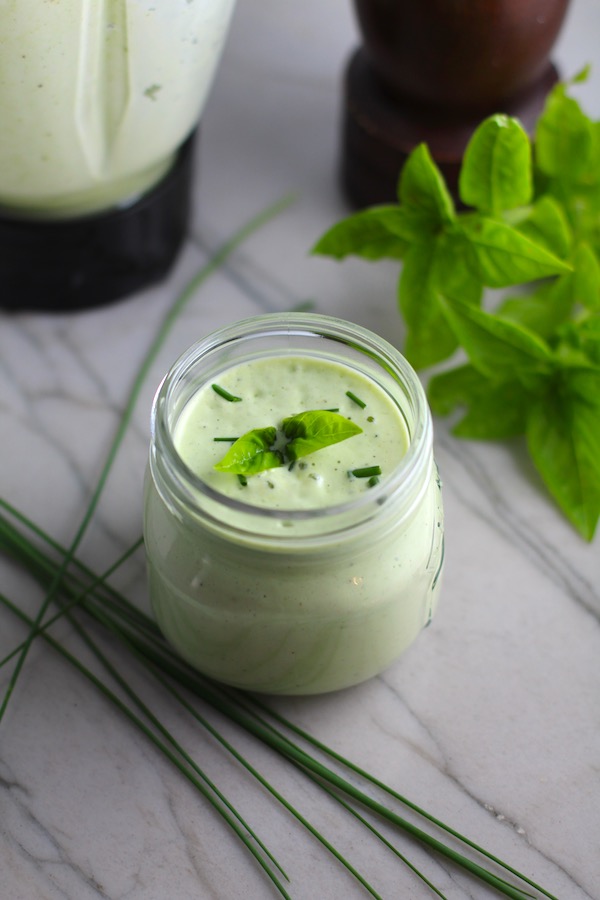 Basil & Chive Yogurt Dressing in a jar on counter with basil leaves and chives on top and on the counter. This dressing with Lemon and Honey is creamy, light, savory, and a little bit sweet. It takes only minutes to make this delicious homemade dressing.  Basil & Chive Yogurt Dressing is perfect for salads, for drizzling over roasted veggies, steak, chicken, or fish, and amazing for dipping fries into!!