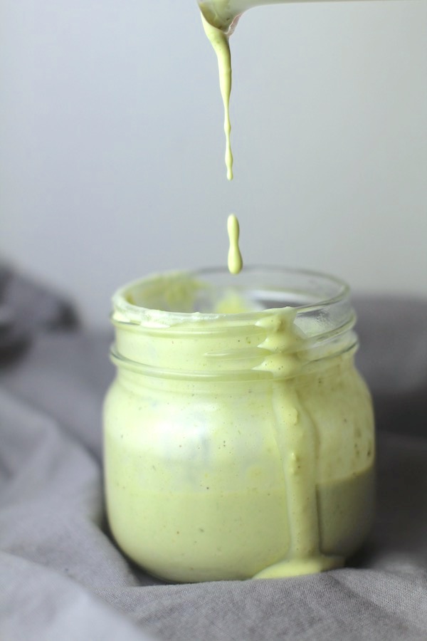 Basil & Chive Yogurt Dressing dripping into a jar sitting on a gray napkin. This dressing with Lemon and Honey is creamy, light, savory, and a little bit sweet. It takes only minutes to make this delicious homemade dressing.  Basil & Chive Yogurt Dressing is perfect for salads, for drizzling over roasted veggies, steak, chicken, or fish, and amazing for dipping fries into!!
