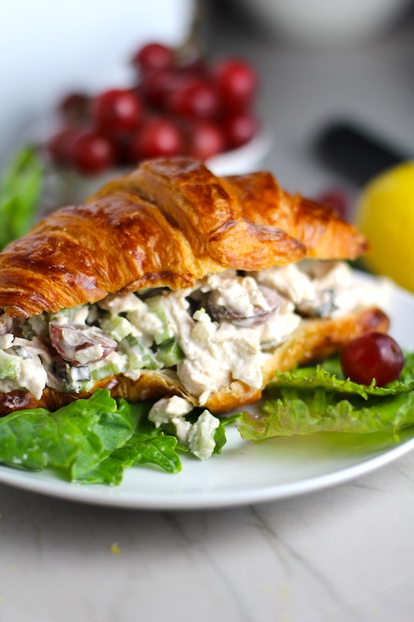 Lemon Basil Chicken Salad with Grapes on a croissant on plate with lettuce and grapes in background. This recipe is simple, but the taste is anything but simple. It has layers of flavors and textures. You get the hearty texture of the chicken, brightness from the lemon, the fresh and fragrant basil, a slight bite from the onion, and a huge juicy burst of sweetness from the grapes.