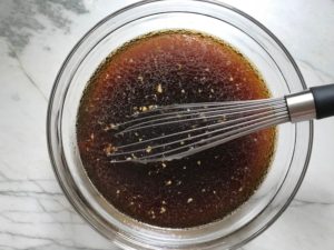 Sauce in clear bowl with whisk for Korean Rice Bowl with Lentils and Cauliflower recipe, which is da bomb, exploding with flavor! The rice soaks up the sauce, which gives you a nutty, salty flavor from sesame oil and soy sauce, a warm and zesty kick from ginger and garlic, and sweetness from honey to balance it all out. Lentils and cauliflower give a meaty bite.