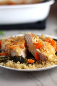 Close up of Smothered Pork Chop cut in half on quinoa with carrots and kale. This casserole is a true midwestern comfort dish with layers of vegetables and meaty pork chops smothered in a creamy sauce and cheese.  The pork chops in this delicious casserole are left whole so that you get an entire portion dripping in goodness in one scoop.