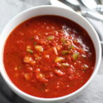 This Roasted Red Pepper Gazpacho recipe is Summer in a bowl - cool, tangy, crunchy, fresh, and creamy. The base is tomato, but this Gazpacho recipe puts Roast Red Pepper in the starring role, which brings another layer of creamy sweetness. Then you get the crunch from the green pepper, cucumber, garlic and scallions.