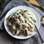 Walnut Cream Sauce mixed with fettuccine and spinach on a plate with a fork. This Walnut Sauce recipe with Ricotta and Spinach is thick, rich, nutty, and creamy.  It's inspired by the traditional Italian Walnut Sauce from the North-Western Italy, Liguria Region, but my Walnut Sauce recipe adds even more decadence with creamy ricotta and more nutty parmesan cheese.