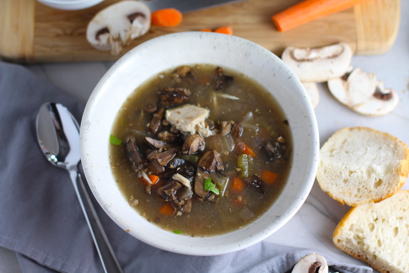 Chicken and Mushroom Soup in white bowl with raw mushrooms, carrots, wood cutting board, bread, and spoon on counter. This Slow Cooker Chicken and Mushroom Soup is warm, hearty, comforting, earthy, and just devine. The mix of blended and chunky mushrooms with carrots, onions, celery, shredded chicken, and herbs gives you a perfect bite every time.