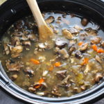 Cooked chicken and mushroom soup in slow cooker with wood spoon. This Slow Cooker Chicken and Mushroom Soup is warm, hearty, comforting, earthy, and just devine. The mix of blended and chunky mushrooms with carrots, onions, celery, shredded chicken, and herbs gives you a perfect bite every time.