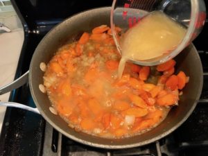 Chicken Broth being poured over carrots and onions in skillet. Smothered Pork Chop Casserole is a true midwestern comfort dish with layers of vegetables and meaty pork chops smothered in a creamy sauce and cheese.  The pork chops in this delicious casserole are left whole so that you get an entire portion dripping in goodness in one scoop.