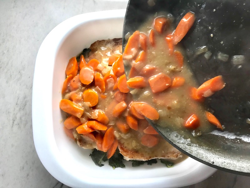 Carrots and Sauce being poured from skillet to casserole dish over pork chops. Smothered Pork Chop Casserole is a true midwestern comfort dish with layers of vegetables and meaty pork chops smothered in a creamy sauce and cheese.  The pork chops in this delicious casserole are left whole so that you get an entire portion dripping in goodness in one scoop.