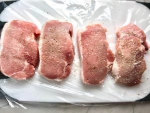 4 raw pork chops seasoned with salt and pepper on plastic wrap on cutting board. Smothered Pork Chop Casserole is a true midwestern comfort dish with layers of vegetables and meaty pork chops smothered in a creamy sauce and cheese.  The pork chops in this delicious casserole are left whole so that you get an entire portion dripping in goodness in one scoop.
