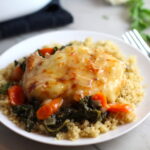 Pork Chop with cheese melted on top over carrots and kale on top of quinoa on plate on counter with casserole dish in background. Smothered Pork Chop Casserole is a true midwestern comfort dish with layers of vegetables and meaty pork chops smothered in a creamy sauce and cheese.  The pork chops in this delicious casserole are left whole so that you get an entire portion dripping in goodness in one scoop.