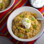 2 Bowls of Chipotle Chicken Enchilada Stew on red napkin with sour cream and scallion slices as garnish. It's one of my Prepped Freezer Meal recipes and it's creamy, cozy, hearty, cheesy, and slightly spicy. All ingredients freeze raw, thaw, then cook in the slow cooker or in the oven. It's a stew because it's thick and hearty with bites of chicken, carrots, onion, chipotle peppers, cumin, garlic and tortilla chips that melt down to thicken this delicious stew.