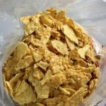 Crushed tortilla chips added to freezer bag for Chipotle Chicken Enchilada Stew. It is one of my Prepped Freezer Meal recipes and it's creamy, cozy, hearty, cheesy, and slightly spicy. All ingredients freeze raw, thaw, then cook in the slow cooker or in the oven. It's a stew because it's thick and hearty with bites of chicken, carrots, onion, chipotle peppers, cumin, garlic and tortilla chips that melt down to thicken this delicious stew.