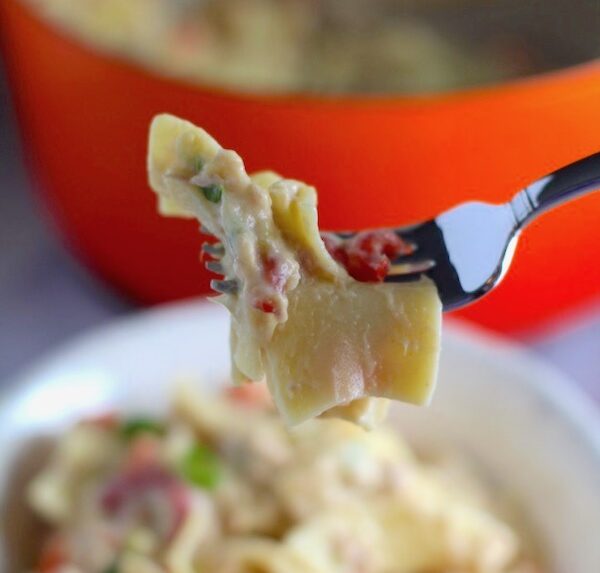 Cheesy Tuna Noodle Casserole Recipe bite on a fork over a bowl with pot in background. This is a creamy and delicious comfort dish with tuna and noodles and a surprise pop of sweet from Pimiento.  This easy recipe is completely from scratch (no canned soup here!) but I can promise you it's so easy and only takes 30 minutes because it's a Casserole that you can make entirely on the stove top!