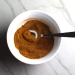 Final Pumpkin Spice Blend in a white bowl with spoon on counter. Recipe has 4 simple ingredients and takes minutes to make! PLUS, here are 20 EASY WAYS TO USE this Spice blend, many with no baking at all!
