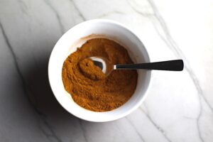Final Pumpkin Spice Blend in a white bowl with spoon on counter. Recipe has 4 simple ingredients and takes minutes to make! PLUS, here are 20 EASY WAYS TO USE this Spice blend, many with no baking at all!