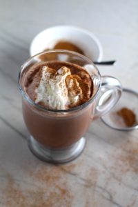 Pumpkin Spice sprinkled on top of whipped cream on hot cocoa. Spice blend in a sifter to the right and in a bowl in background. Recipe has 4 simple ingredients and takes minutes to make! PLUS, here are 20 EASY WAYS TO USE this Spice blend, many with no baking at all!