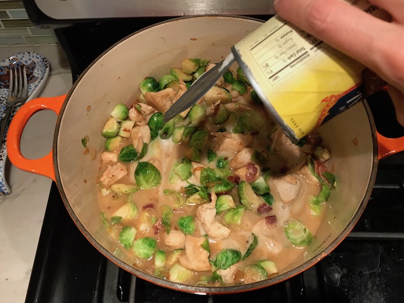 Adding Coconut Milk to brussel sprouts and chicken in pot for the Easy Bacon Brussel Sprouts and Chicken recipe. It's a perfect quick Fall Recipe!  It has a creamy sauce filled with salty bacon, earthy and almost nutty seared brussel sprouts, and hearty healthy chicken. Serve over rice (or Quinoa or pasta!).
