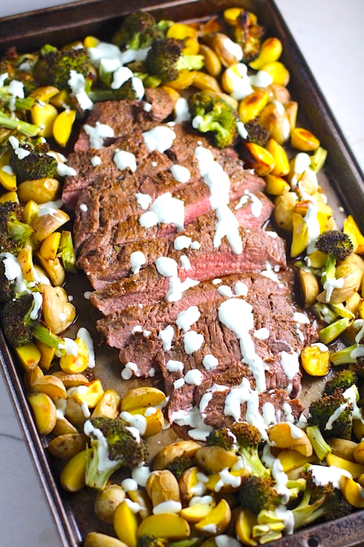Flank Steak sliced with Potatoes & Broccoli on sheet pan with crema drizzled on top. This Flank Steak Broccoli and Potatoes dinner is an easy and delicious Sheet Pan recipe.