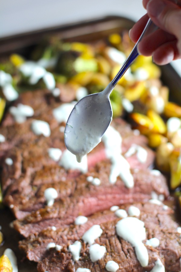 Spoon drizzling crema over sliced Flank Steak broccoli and Potatoes on sheet pan. This is an easy and delicious Sheet Pan Dinner.  