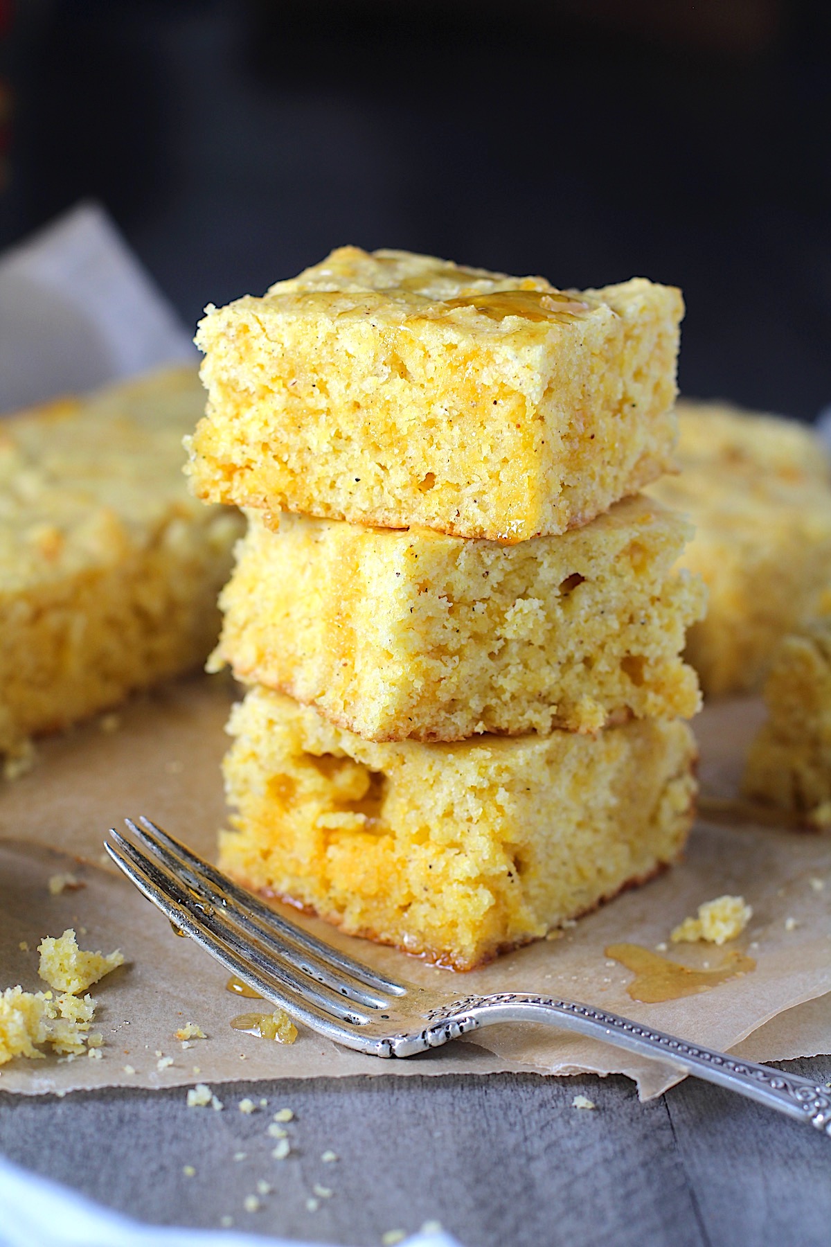 Cheddar Honey Glazed Cornbread pieces stacked on parchment paper with honey drizzled on top and fork and crumbs around.