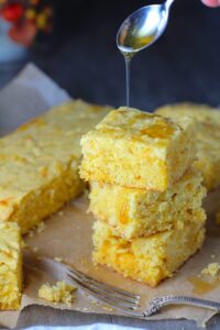 Cheddar Honey Gluten Free Cornbread pieces stacked on parchment paper with honey drizzled on top and fork and crumbs around.