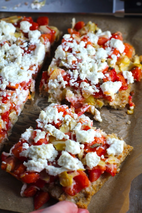 Close up of cut Tomato Tart on parchment. It gives you crunch from the Quinoa crust, a burst of fresh from the tomatoes, tons of flavor from the basil and garlic, tang and meatiness from the artichoke and so much creaminess from the mozzarella and goat cheese!  It's addictive and delicious!