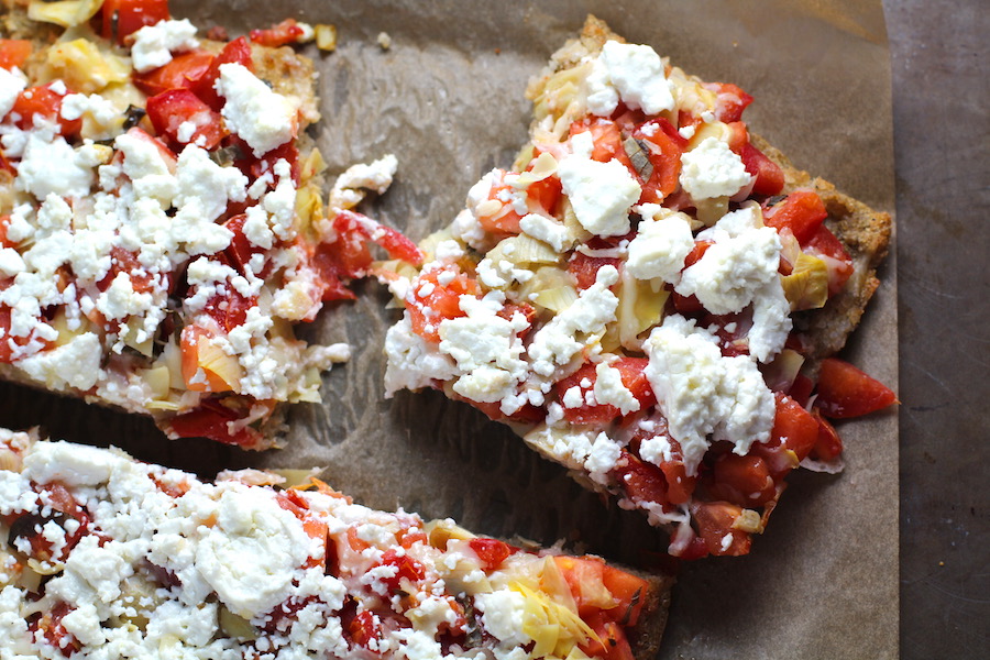 Close up of cut Tomato Tart on parchment. It gives you crunch from the Quinoa crust, a burst of fresh from the tomatoes, tons of flavor from the basil and garlic, tang and meatiness from the artichoke and so much creaminess from the mozzarella and goat cheese!  It's addictive and delicious!