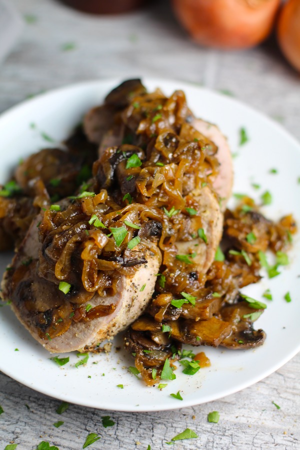 Caramelized Onions & Mushrooms on sliced Pork Tenderloin on a white plate with parsley sprinkled over top.  This is such a flavorful main dish!  The pork tenderloin is moist and juicy and topped with Onions & Mushrooms that are sauteed low and slow with a touch of balsamic to bring out all of the natural sugars and caramelize them to perfection.