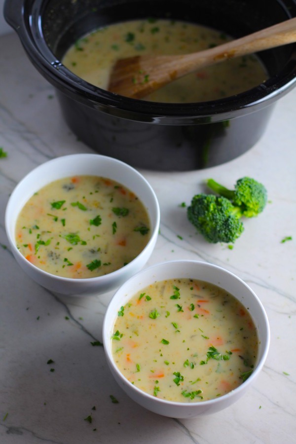 Slow Cooker Creamy Broccoli Soup in two boels on counter with crockpot in back.  This is easy, comforting, and delicious!  With Carrots, Broccoli, Onion, Garlic, and Oregano, this is one flavorful soup.  And, there is no heavy cream, just milk and a little half and half mixed with cornstarch, so it's healthy and gluten free!