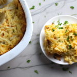 Cheesy Hash Brown Casserole on plate and in casserole dish on counter. This recipe does not disappoint! It's warm, creamy, and full of flavor! And it's the perfect side dish for your holiday dinner.