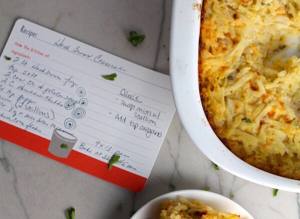 Cheesy Hash Brown Casserole without soup from a can on plate and in casserole dish on counter with recipe card. This recipe does not disappoint! It's warm, creamy, and full of flavor! And it's the perfect side dish for your holiday dinner.