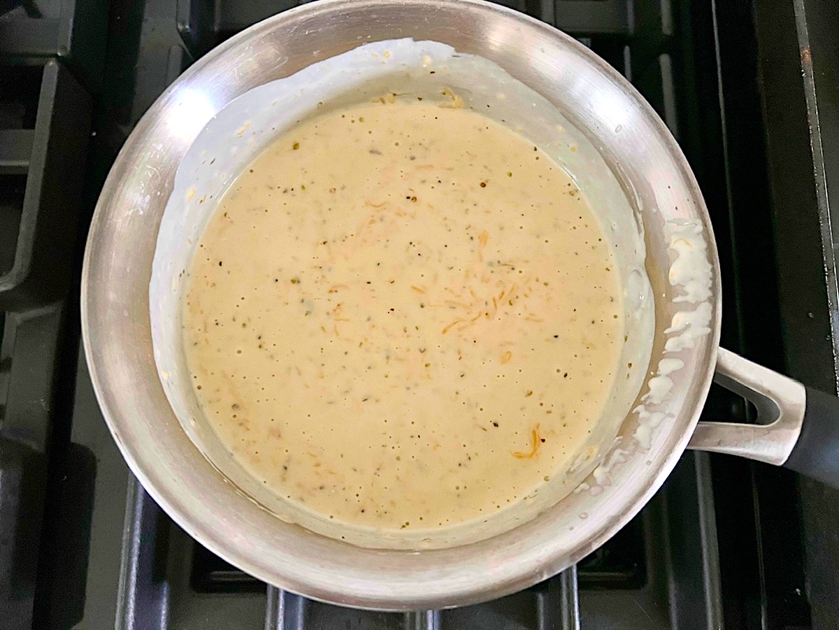 Shredded cheddar cheese mixed into, but not completely melted, the sauce in a saucepan on the stove for Hash Brown Casserole without Soup.