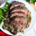 Stuffed Flank Steak cooked and cut on white plate with stuffing oozing out and basil on side. In the stuffing you get mushrooms, onions, and garlic sauteed together. Then they are mixed with fresh parsley and basil, then parmesan, and goat cheese! Roll it all up in Flank Steak and roast for an amazing dinner.