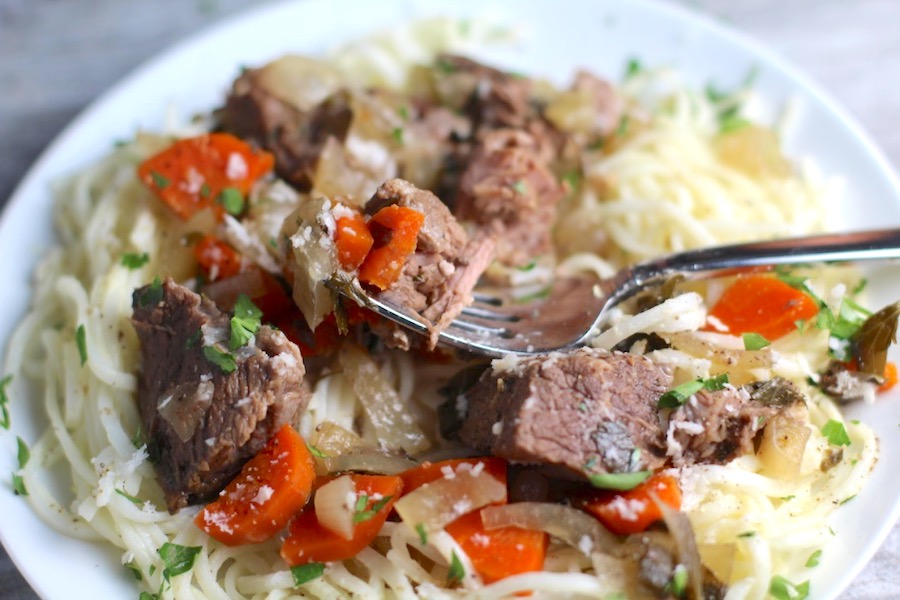 Slow Cooker Beef Stew over Noodles on a plate with fork. This is downhome comfort food that's full of flavor and texture with carrots, onion, garlic, thyme, beef, and more. Now, try pouring that salty, chunky, saucy goodness over noodles...yup, even more amazing!#beefstew #crockpot #slowcooker #easydinners #dinnerrecipes