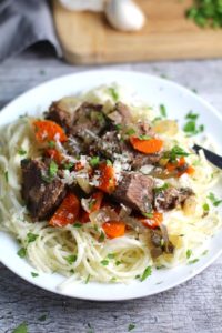 Slow Cooker Beef Stew over Noodles on a plate. This is downhome comfort food that's full of flavor and texture with carrots, onion, garlic, thyme, beef, and more. Now, try pouring that salty, chunky, saucy goodness over noodles...yup, even more amazing! #beefstew #crockpot #slowcooker #easydinners #dinnerrecipes