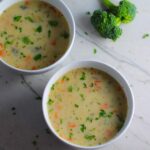 Slow Cooker Creamy Broccoli Soup in two bowls on counter with crockpot in back. This is easy, comforting, and delicious! With Carrots, Broccoli, Onion, Garlic, and Oregano, this is one flavorful soup. And, there is no heavy cream, just milk and a little half and half mixed with cornstarch, so it's healthy and gluten free!