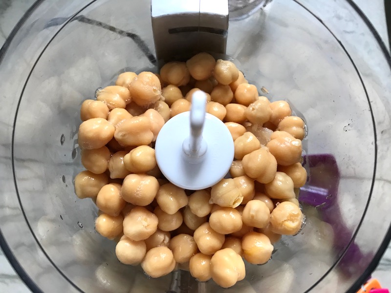 Whole Chickpeas in food processor for Magical Sriracha Hummus. This recipe is seriously the easiest hummus you will ever make and it's perfect for snacking or adding to a meal. The chickpeas have so much flavor and the Sriracha gives it a kick that is totally addictive!
