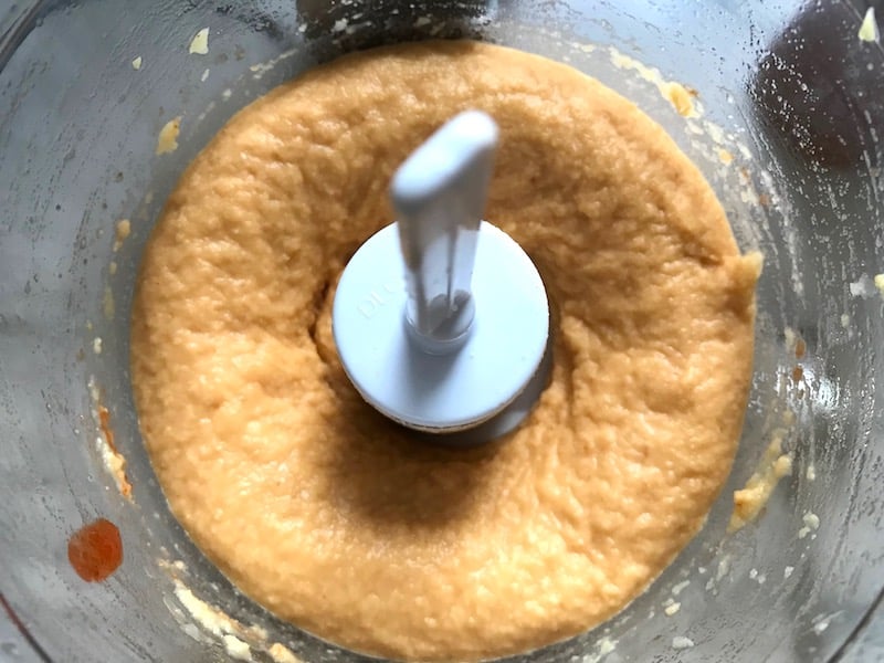 Blended Chickpeas and Sriracha in food processor for Magical Sriracha Hummus. This recipe is seriously the easiest hummus you will ever make and it's perfect for snacking or adding to a meal. The chickpeas have so much flavor and the Sriracha gives it a kick that is totally addictive!