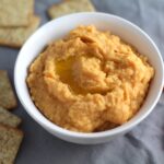 2-Ingredient Magical Sriracha Hummus in a bowl with crackers and carrots next to it. This is seriously the easiest hummus you will ever make and it's perfect for snacking or adding to a meal.  The chickpeas have so much flavor and the Sriracha gives it a kick that is totally addictive!