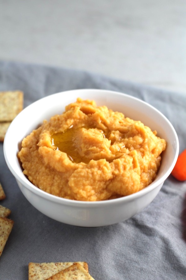 2-Ingredient Magical Sriracha Hummus in a bowl with crackers and carrots next to it. This is seriously the easiest hummus you will ever make and it's perfect for snacking or adding to a meal.  The chickpeas have so much flavor and the Sriracha gives it a kick that is totally addictive!