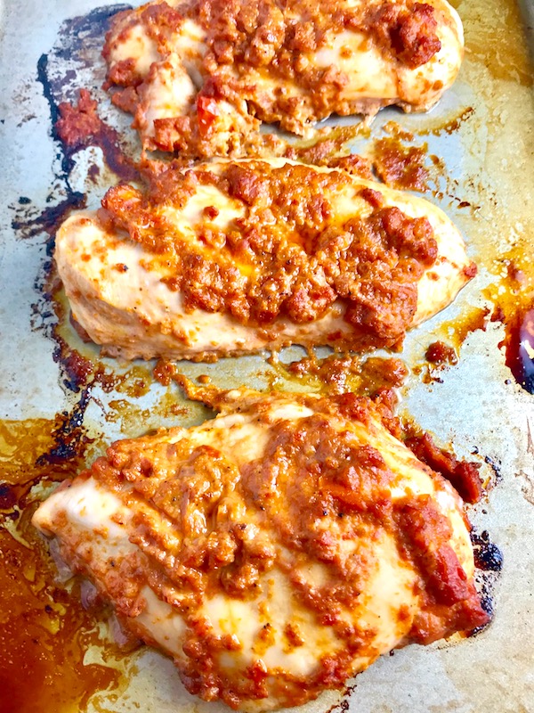 Sun Dried Tomato Chicken breasts cooked on a pan. It's slightly sweet, slightly tart and tangy, and hugely delicious!  When Sun dried tomatoes are rehydrated and blended, they turn into a thick and lucious sauce that coats the chicken keeping it moist and juicy when it simply bakes in the oven.  It's a perfect easy weeknight dinner that you can prepare ahead and cook quickly! #chicken #chickenrecipes #easydinners #dinnerrecipes