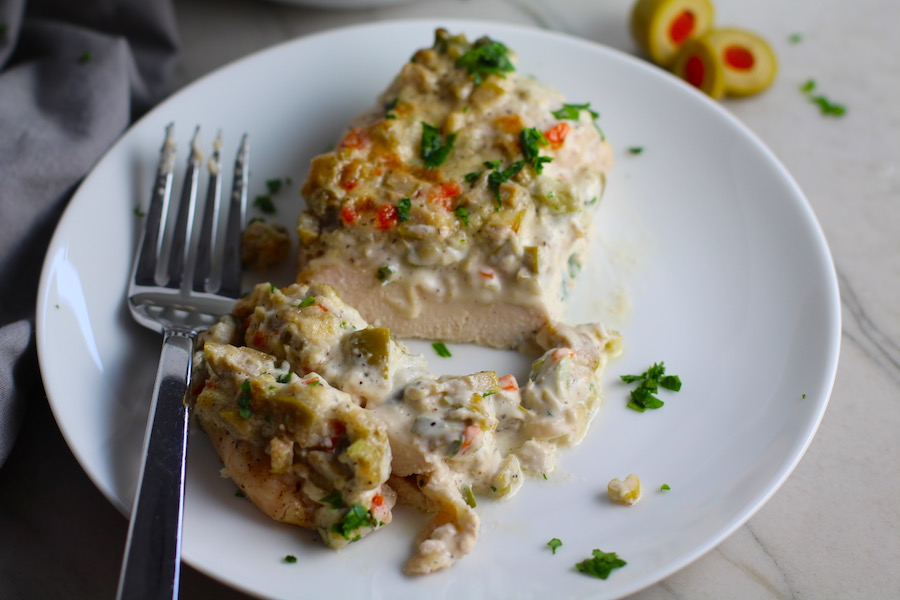 Creamy Olive Chicken cut on plate with fork. This is magnificently thick and creamy and infused with garlic flavor and nuttiness from the Parmesan. The best part; however, is the salty and briny flavor kick from the green olives with a little sweetness from the pimiento. #chicken #chickenrecipes #chickendinner #easydinners #easyrecipes #comfortfood #casserole