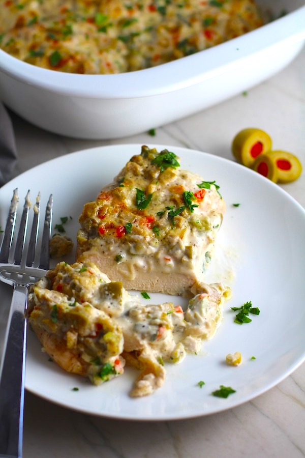 Creamy Olive Chicken cut on plate with fork and casserole dish in background. This is magnificently thick and creamy and infused with garlic flavor and nuttiness from the Parmesan. The best part; however, is the salty and briny flavor kick from the green olives with a little sweetness from the pimiento. #chicken #chickenrecipes #chickendinner #easydinners #easyrecipes #comfortfood #casserole