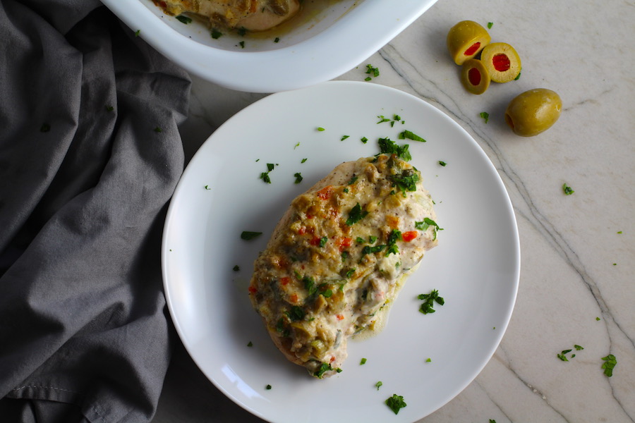 Creamy Olive Chicken on plate with casserole dish in background. This is magnificently thick and creamy and infused with garlic flavor and nuttiness from the Parmesan. The best part; however, is the salty and briny flavor kick from the green olives with a little sweetness from the pimiento. #chicken #chickenrecipes #chickendinner #easydinners #easyrecipes #comfortfood #casserole