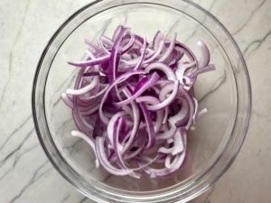 Red Onions in bowl before pickling for Slow Cooker Pork Tacos with with Pickled Onions, Shredded Cheese, and Cilantro Lime Crema drizzled on top!  It's such an easy dinner since the pork cooks in the slow cooker to be perfectly seasoned and fall apart tender. #tacos #easydinner #glutenfree #dinner #mexican #pork