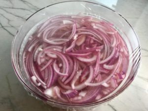 Red Onions pickling in vinegar in bowl for Slow Cooker Pork Tacos with with Pickled Onions, Shredded Cheese, and Cilantro Lime Crema drizzled on top!  It's such an easy dinner since the pork cooks in the slow cooker to be perfectly seasoned and fall apart tender. #tacos #easydinner #glutenfree #dinner #mexican #pork