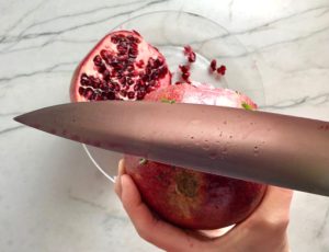 Knife hitting Pomegranate to get seeds out for Quinoa & Kale Salad with Roasted Chickpeas, Pomegranate, Feta, red pepper, and Creamy Lemon Dressing. #glutenfree #lunch #dinner #healthyrecipes #healthyfood #salads #quinoa #kale