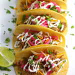 Slow Cooker Pork Tacos with with Pickled Onions, Shredded Cheese, and Cilantro Lime Crema drizzled on top!  It's such an easy dinner since the pork cooks in the slow cooker to be perfectly seasoned and fall apart tender. #tacos #easydinner #glutenfree #dinner #mexican #pork