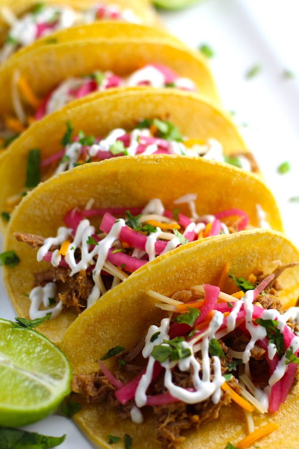 Slow Cooker Pork Tacos with with Pickled Onions, Shredded Cheese, and Cilantro Lime Crema drizzled on top!  It's such an easy dinner since the pork cooks in the slow cooker to be perfectly seasoned and fall apart tender. #tacos #easydinner #glutenfree #dinner #mexican #pork